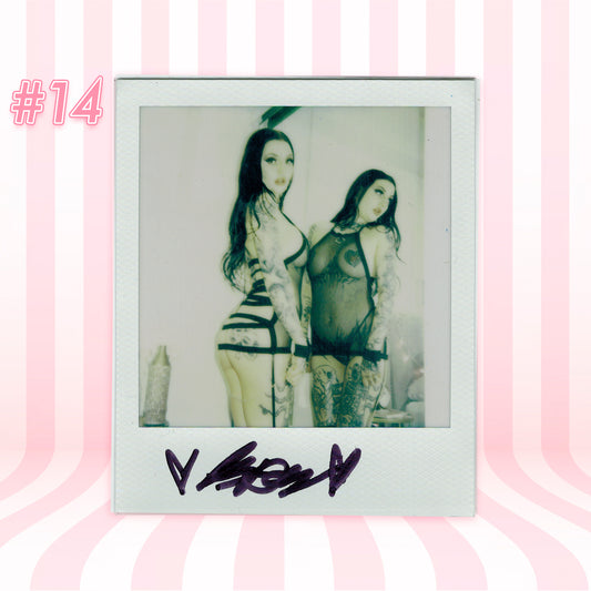 Polaroid-style photo of two people in revealing outfits with a pink striped background.