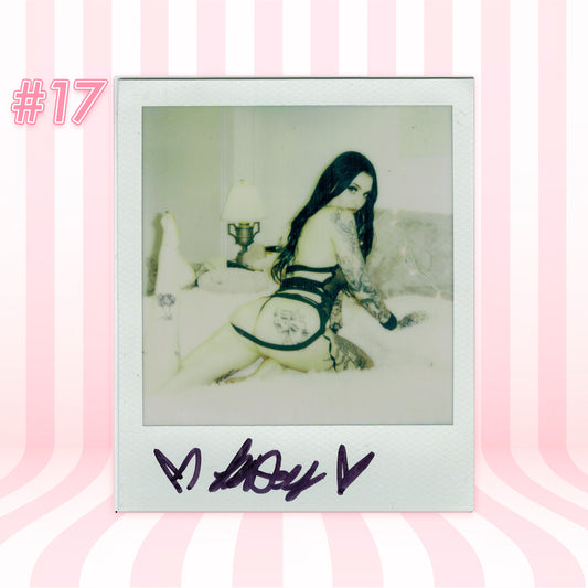 Polaroid-style photo of a person in a suggestive pose with a signature at the bottom, on a pink and white striped background.