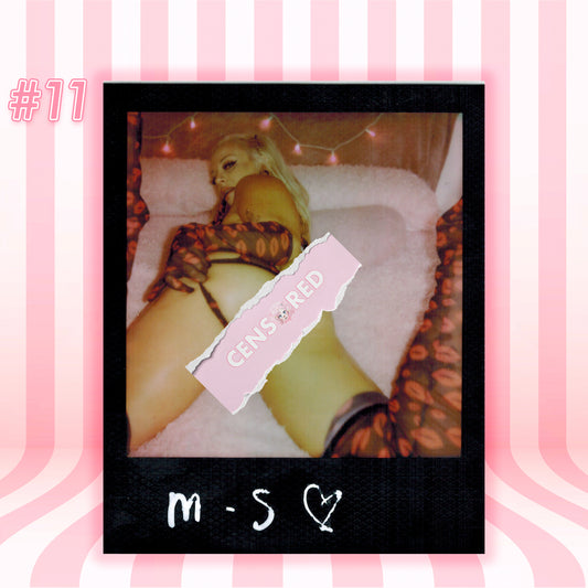 A Polaroid-style photo print centered on a pink striped background. The print shows a censored close-up of a person lying on a bed with string lights, a pink torn label reading 'CENSORED,' and handwritten initials at the bottom.